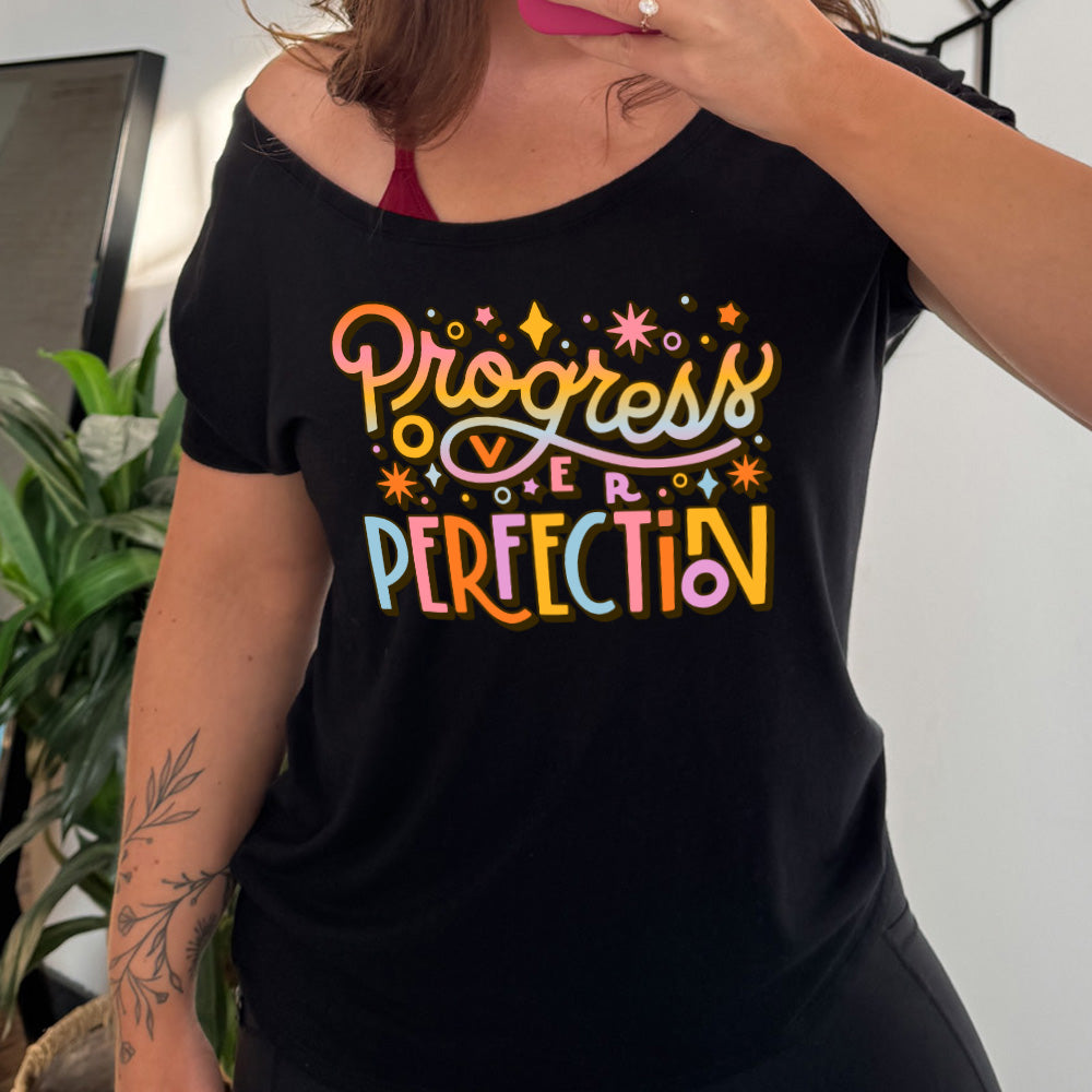 black slouchy tee with the words "Progress Over Perfection" written in colorful lettering, with various stars