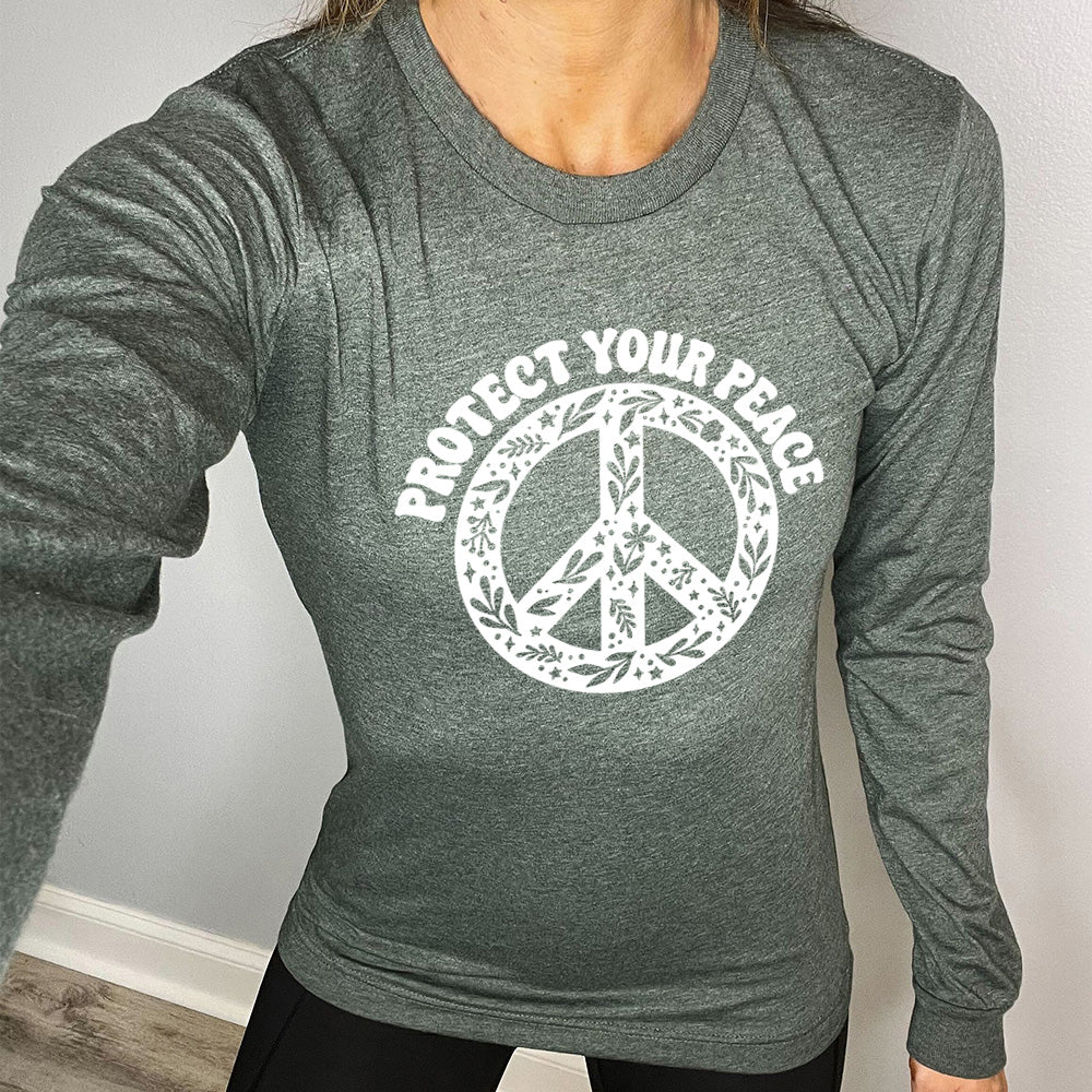 heather forest long sleeve with the text "protect your peace" and a peace sign graphic on it