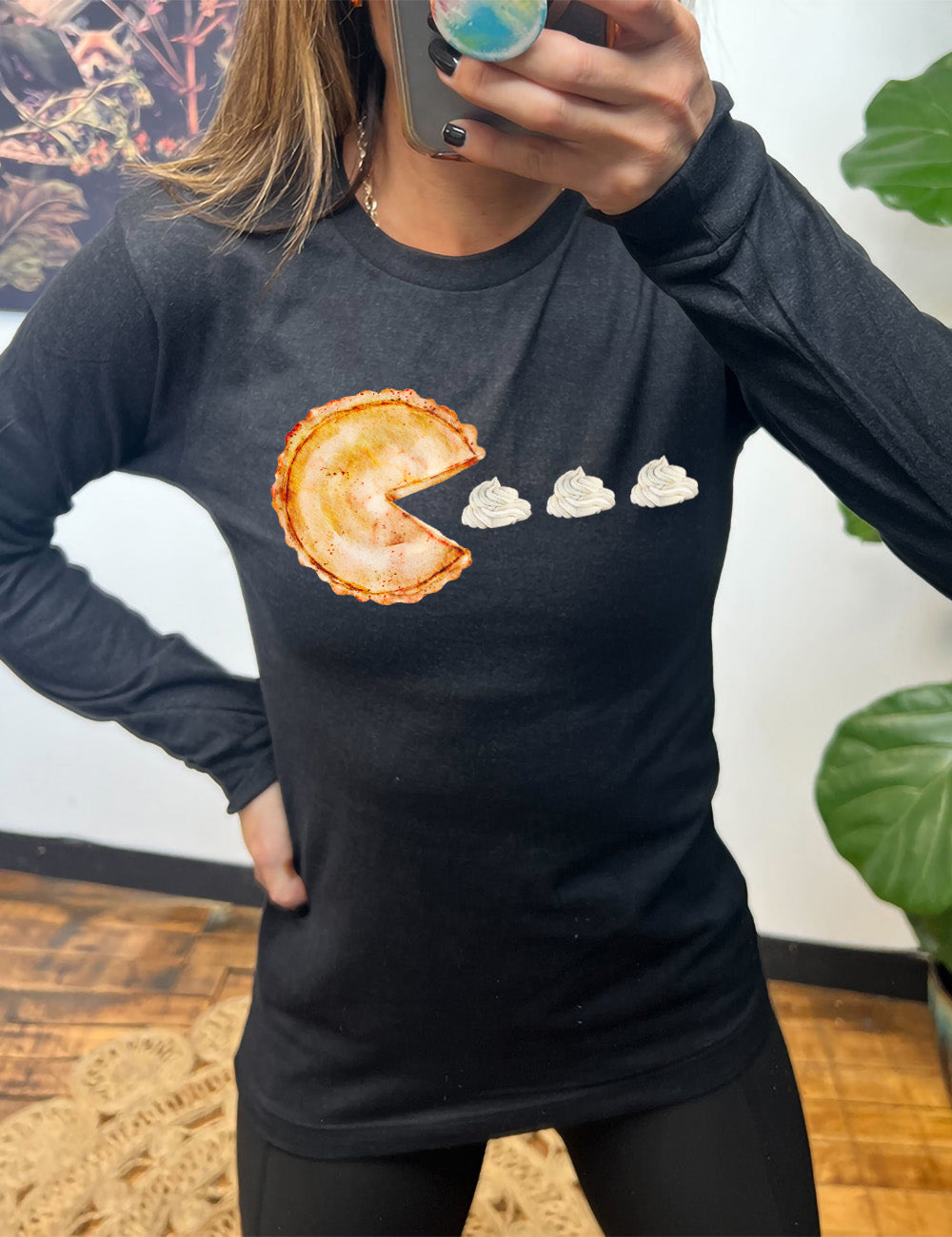 heather black long sleeve tee with the graphic of a pumpkin pie, with the a slice taken out of it so that it looks like Pacman, heading in the direction of three dollops of whipped cream