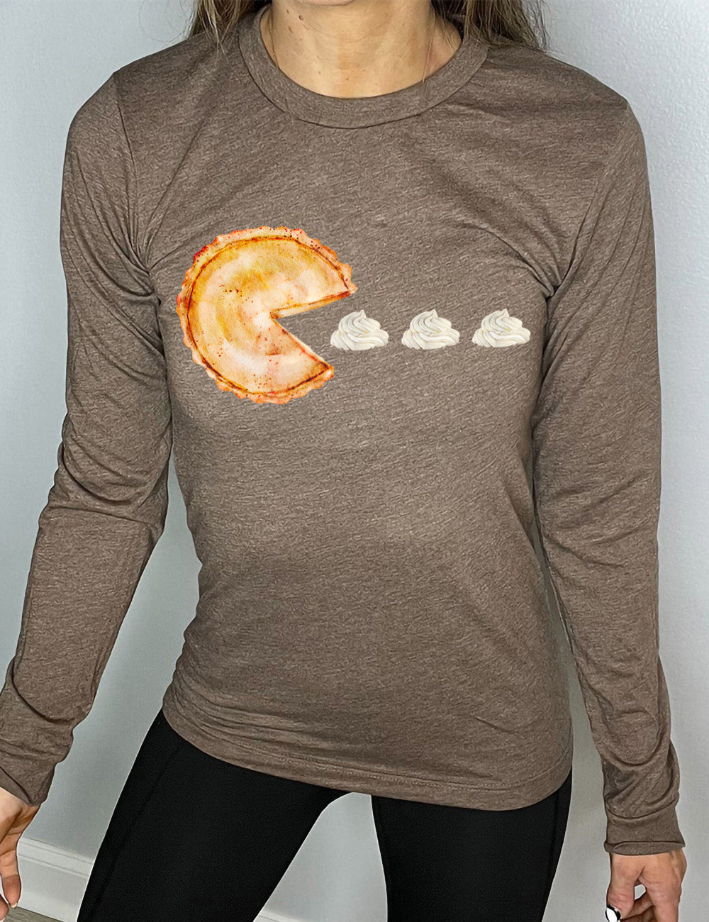 heather brown long sleeve tee with the graphic of a pumpkin pie, with the a slice taken out of it so that it looks like Pacman, heading in the direction of three dollops of whipped cream