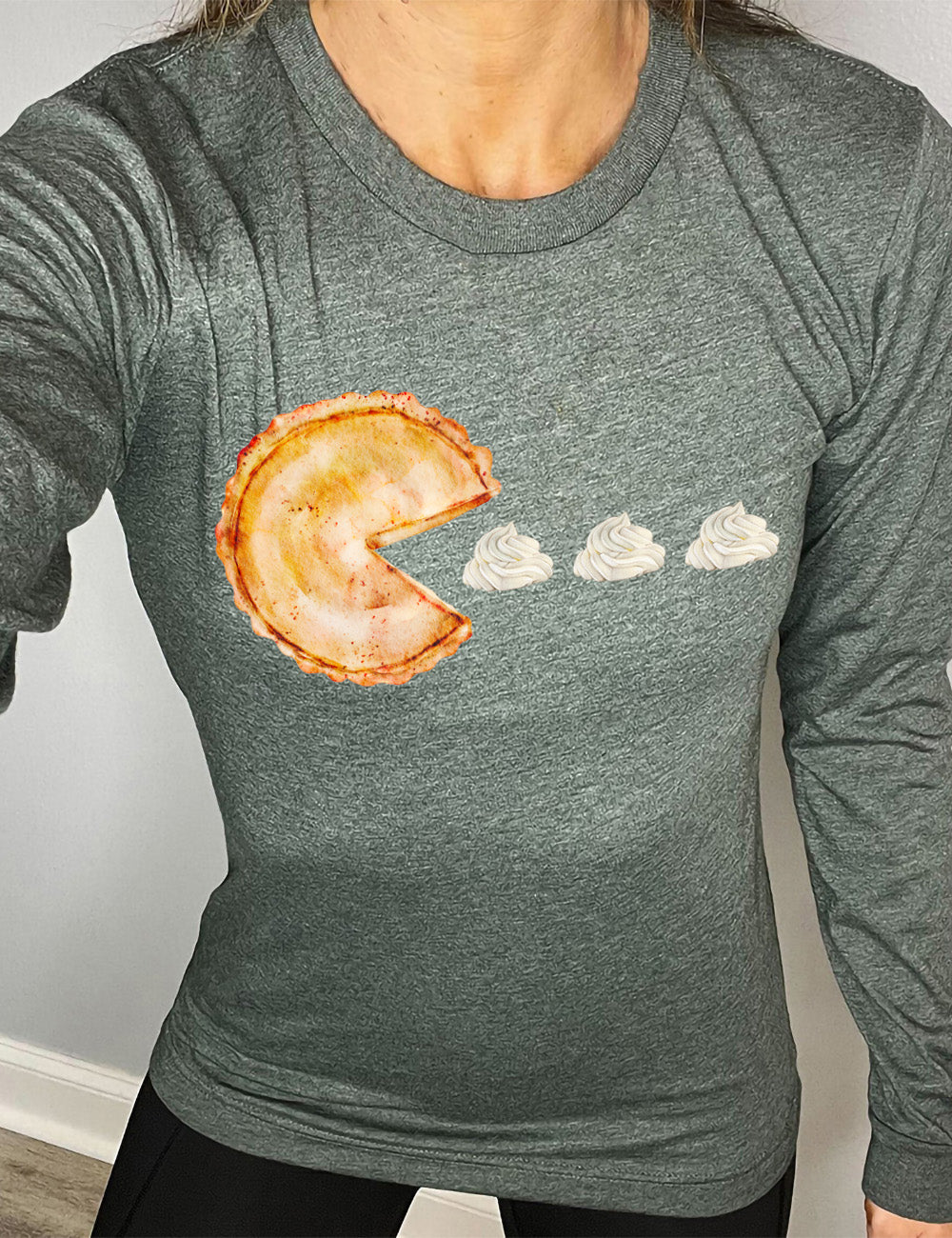 heather forest long sleeve tee with the graphic of a pumpkin pie, with the a slice taken out of it so that it looks like Pacman, heading in the direction of three dollops of whipped cream
