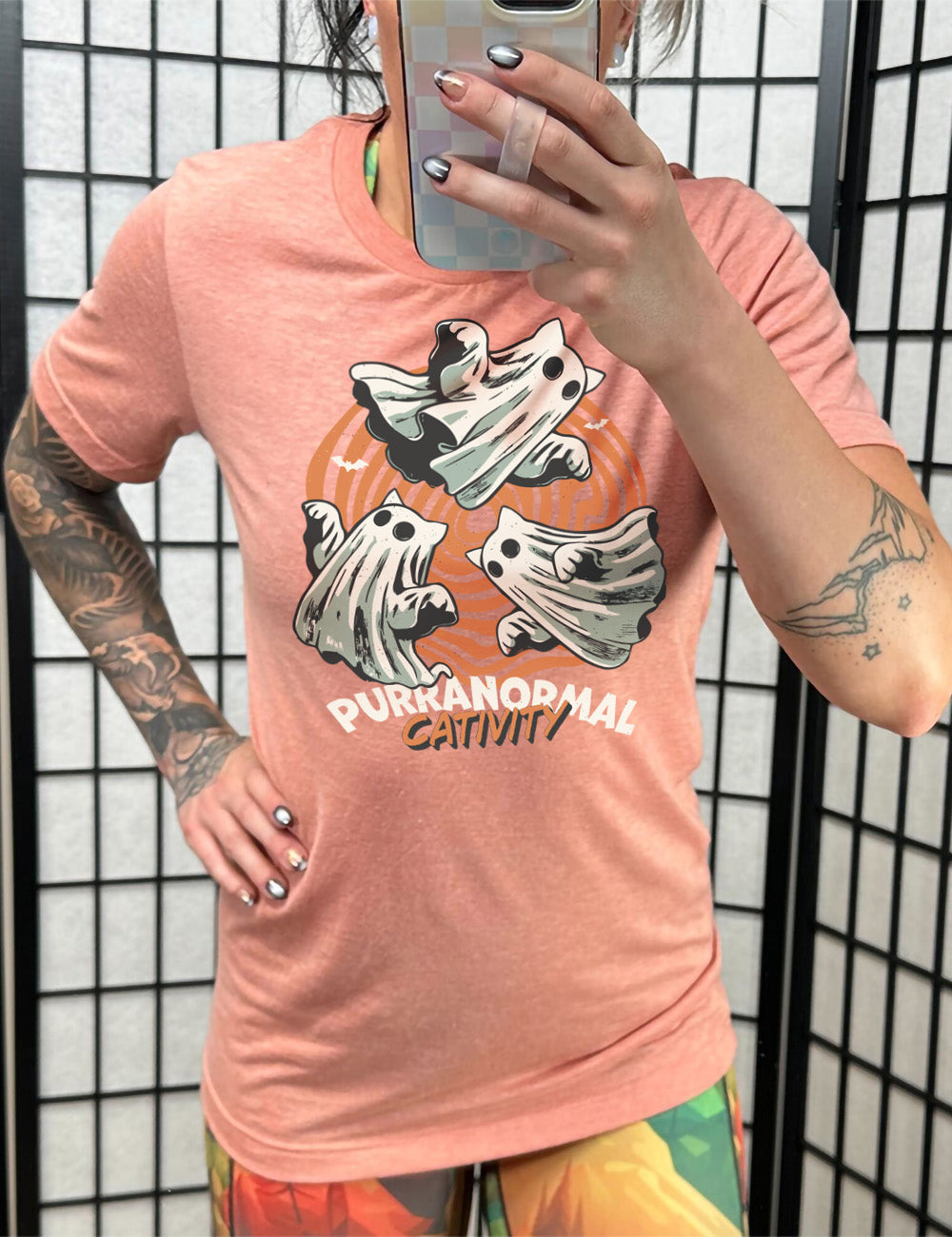 sunset unisex tee with the graphic of three cat-ghosts swirling in a circle, in front of a spiraled background, with words underneath saying "purranormal cativity"