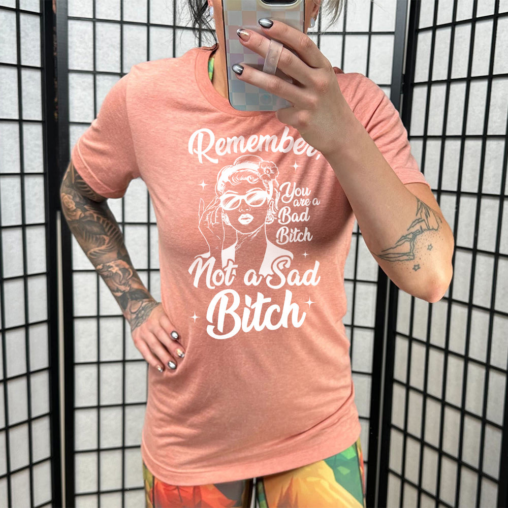 sunset unisex tee with the words "Remember, you are a bad bitch not a sad bitch" with the graphic of a vintage-looking woman adjusting her sunglasses