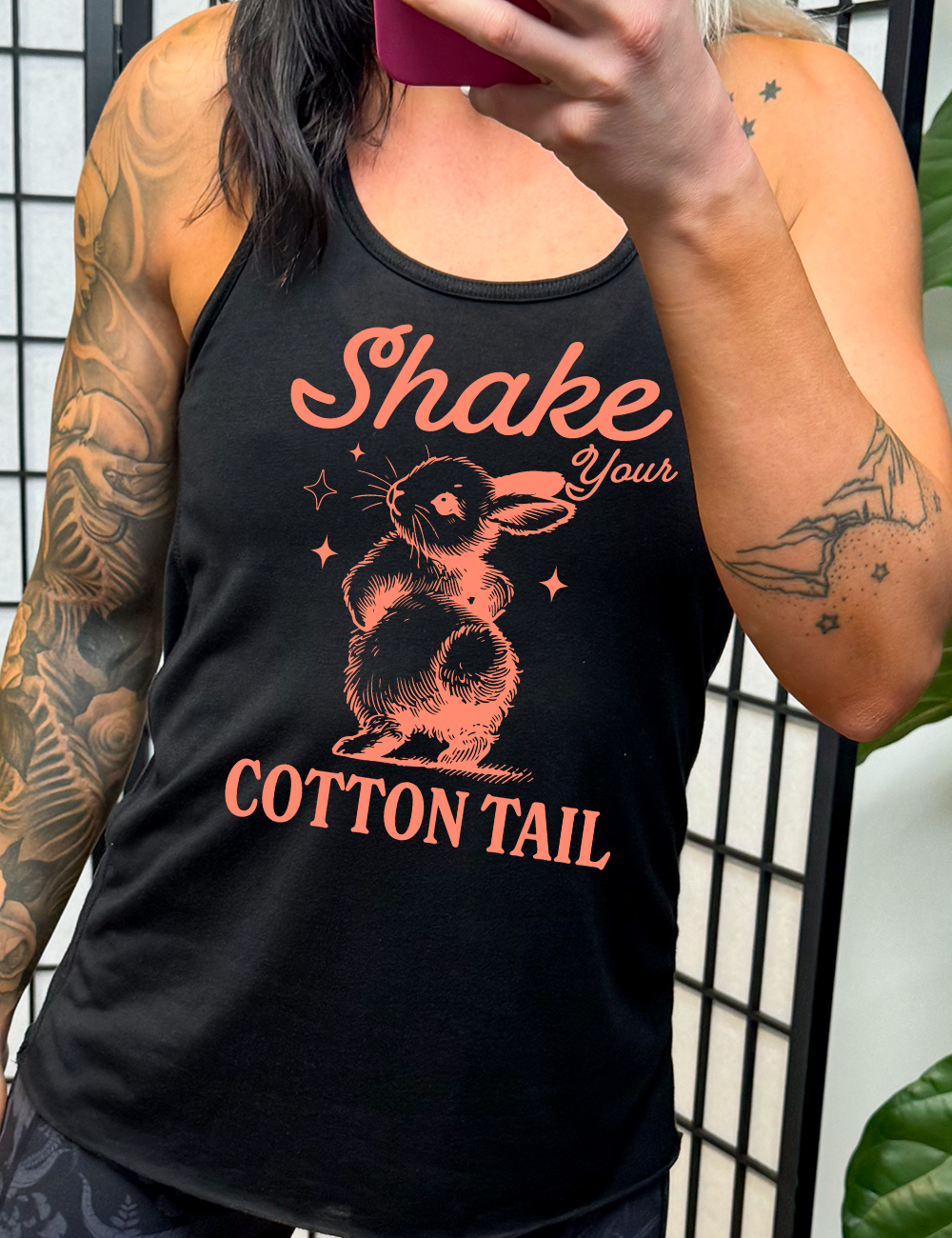 black racerback tank with the words "shake your cotton tail" on it, with the large graphic of a rabbit, mid-shake of its behind, looking over its shoulder