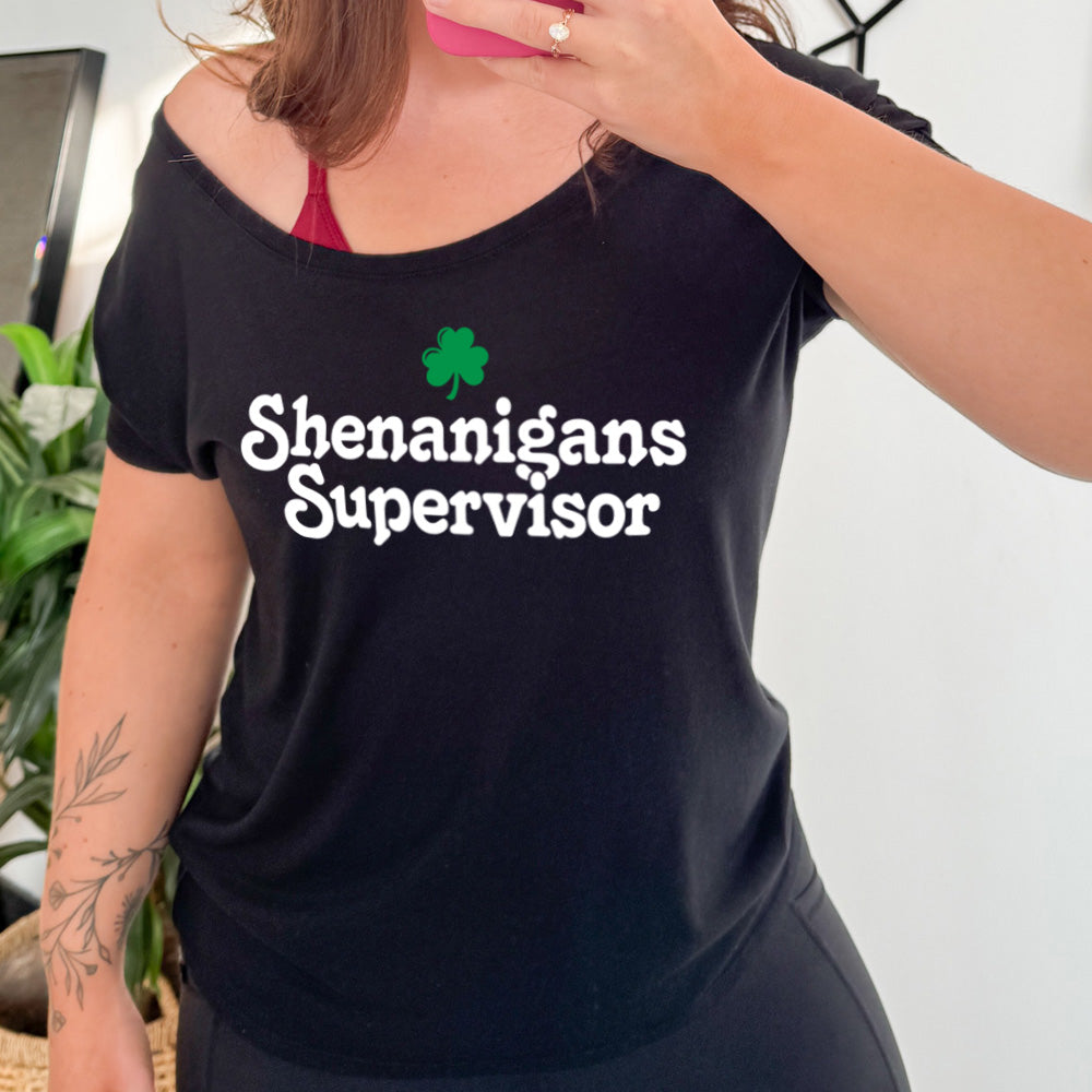 black slouchy tee with the words "shenanigans supervisor" on it, with one small clover graphic above it