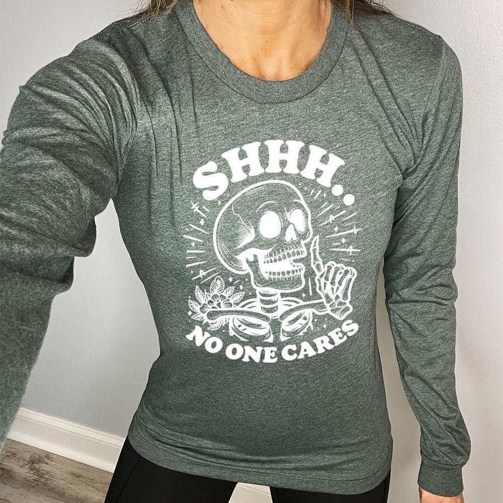 heather forest long sleeve with the words "Shhh.. no one cares" on it, with the graphic of a skeleton holding a finger to its lips 