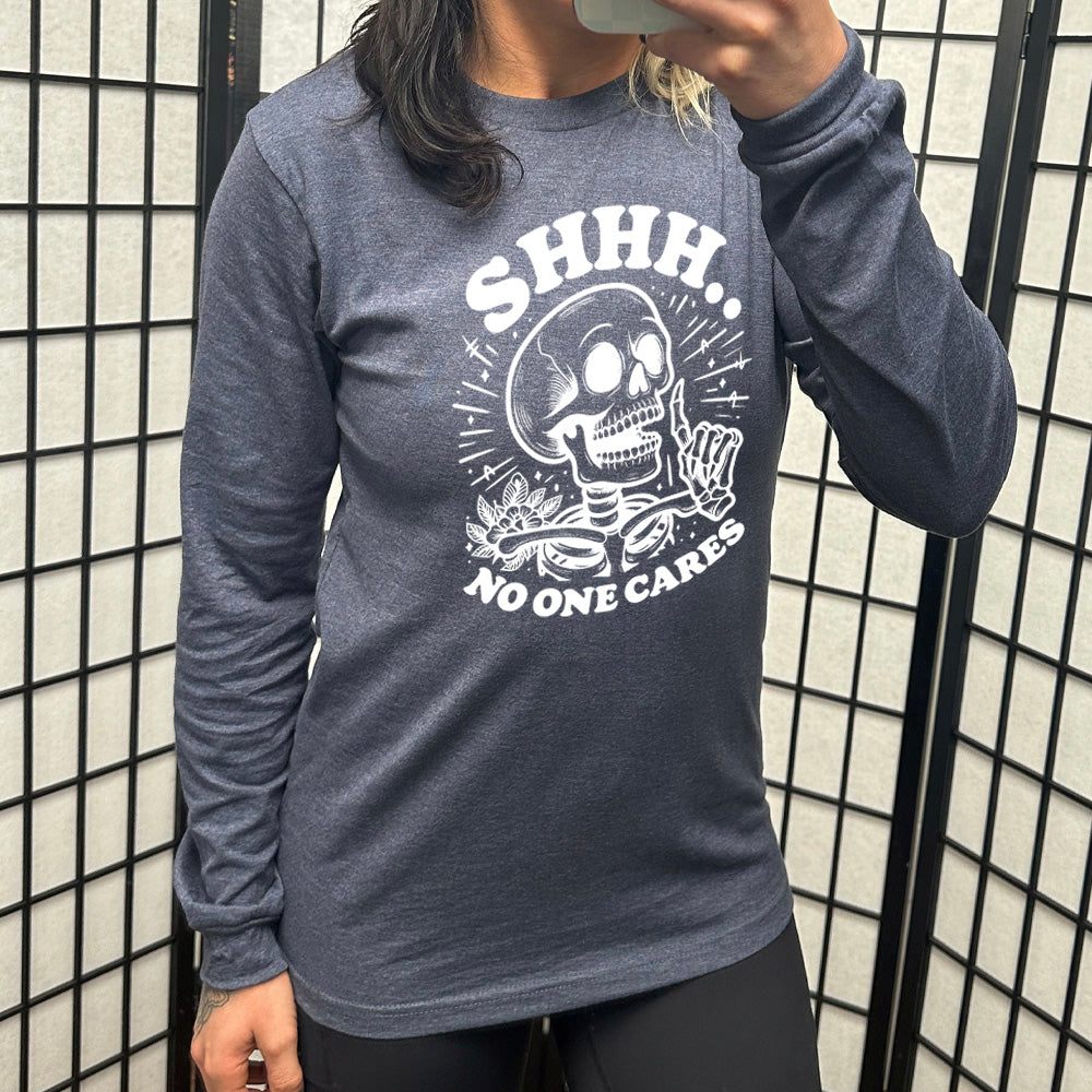 heather navy long sleeve with the words "Shhh.. no one cares" on it, with the graphic of a skeleton holding a finger to its lips 