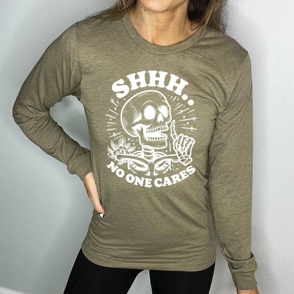 heather olive long sleeve with the words "Shhh.. no one cares" on it, with the graphic of a skeleton holding a finger to its lips 