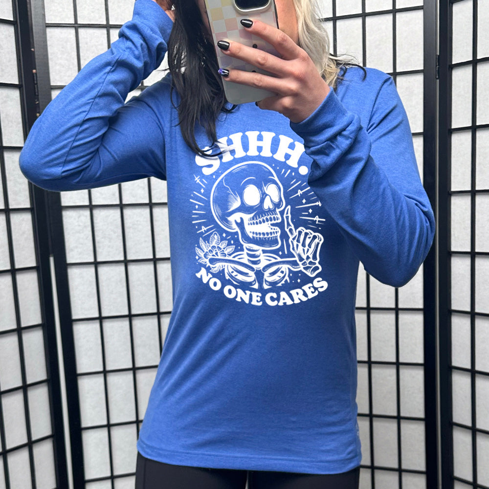 heather true royal long sleeve with the words "Shhh.. no one cares" on it, with the graphic of a skeleton holding a finger to its lips 