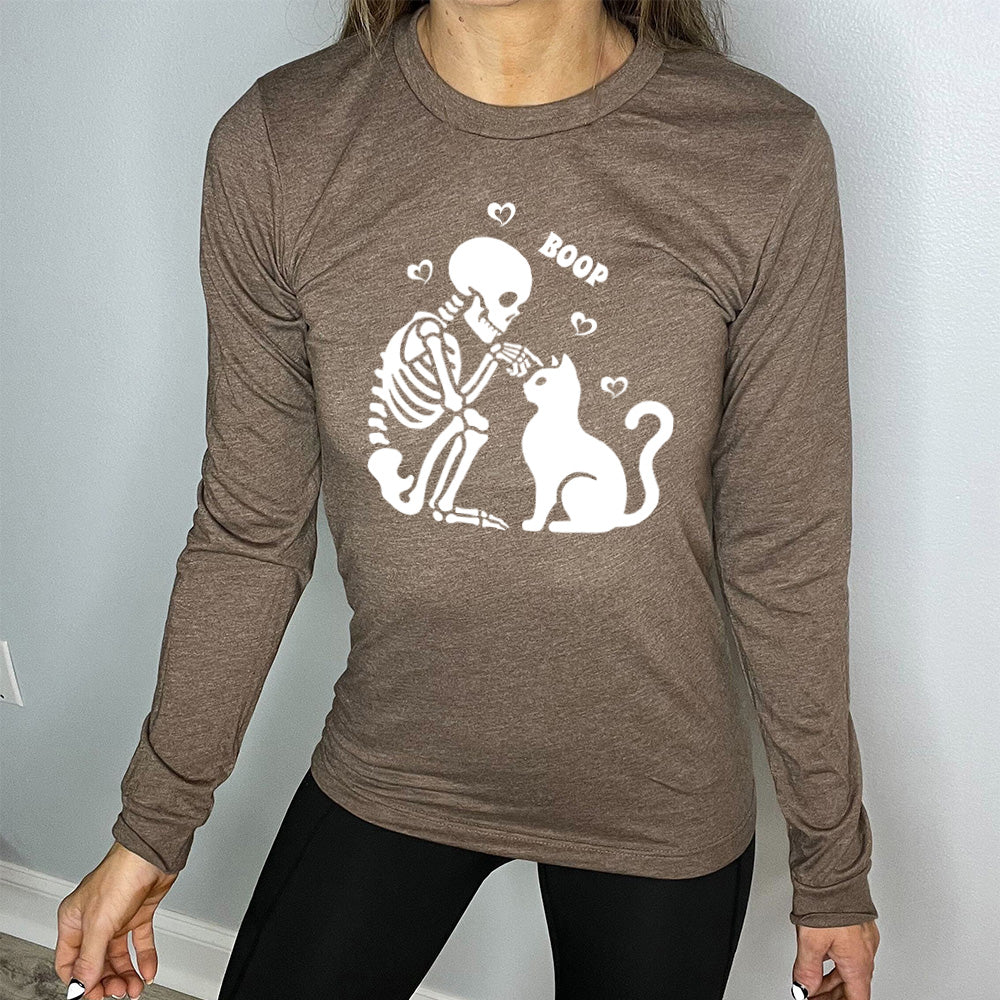 heather brown long sleeve shirt with the graphic of a sitting skeleton touching the head of a sitting cat, with the word "boop" above this action, and four little hearts around them