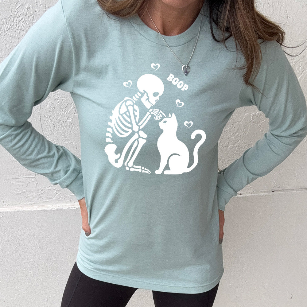 heather dusty blue long sleeve shirt with the graphic of a sitting skeleton touching the head of a sitting cat, with the word "boop" above this action, and four little hearts around them