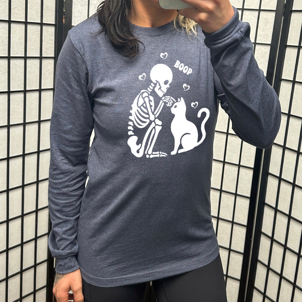 heather navy long sleeve shirt with the graphic of a sitting skeleton touching the head of a sitting cat, with the word "boop" above this action, and four little hearts around them