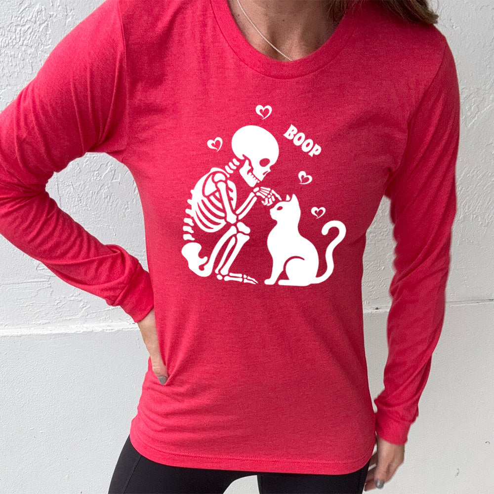 heather red long sleeve shirt with the graphic of a sitting skeleton touching the head of a sitting cat, with the word "boop" above this action, and four little hearts around them