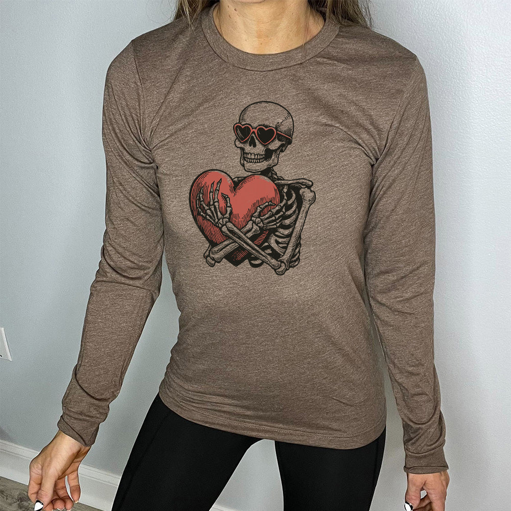 heather brown long sleeve shirt with the graphic of a skeleton, wearing sunglasses, hugging a big heart close