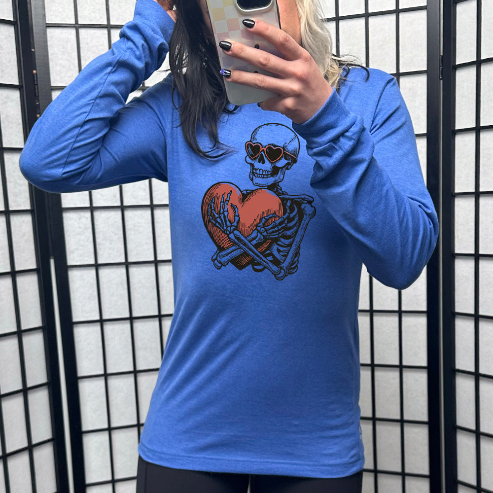 heather true royal long sleeve shirt with the graphic of a skeleton, wearing sunglasses, hugging a big heart close
