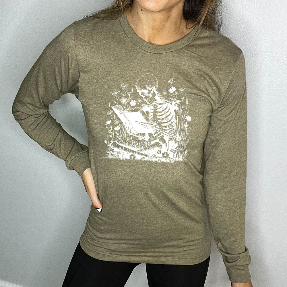 heather olive long sleeve shirt with the graphic of a skeleton reading a book, sitting cross-legged in a bed of tall flowers