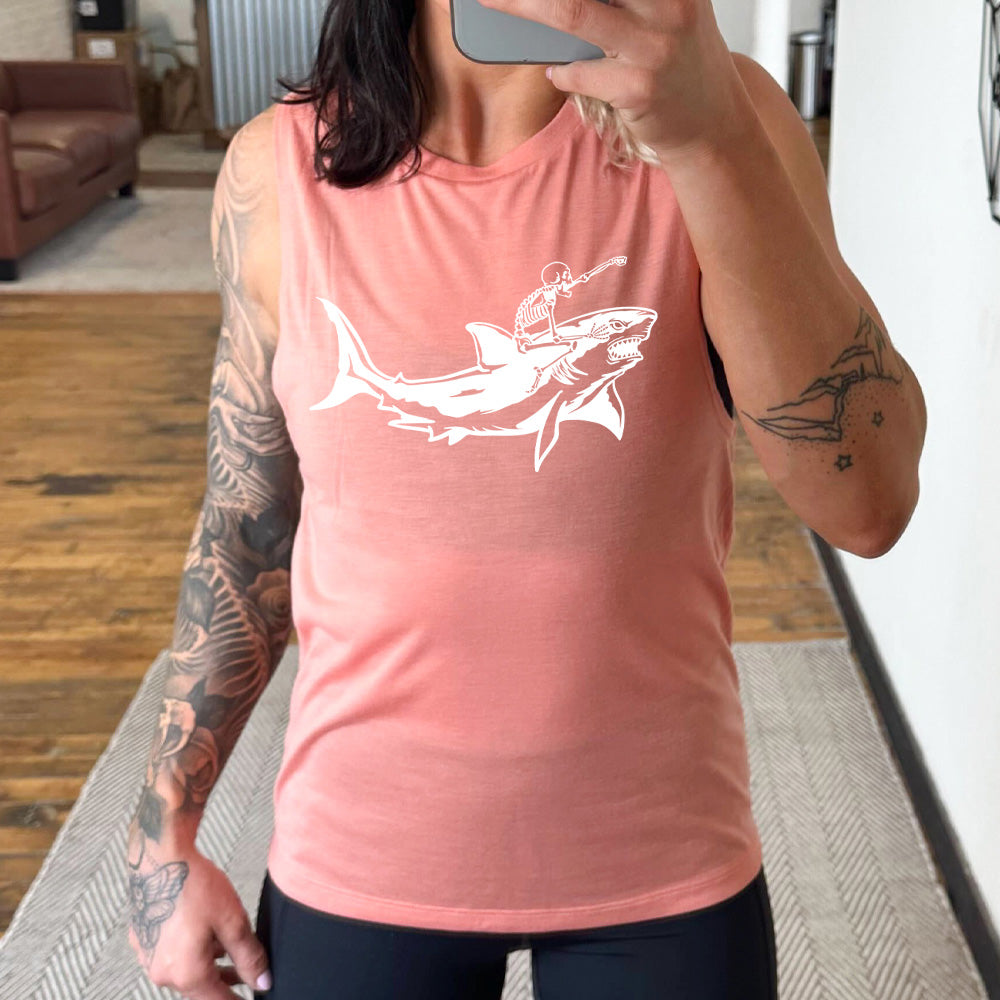 peach muscle tank with the graphic of a skeleton, with its fist pointing onwards and its mouth open, riding a shark, who has a fierce expression