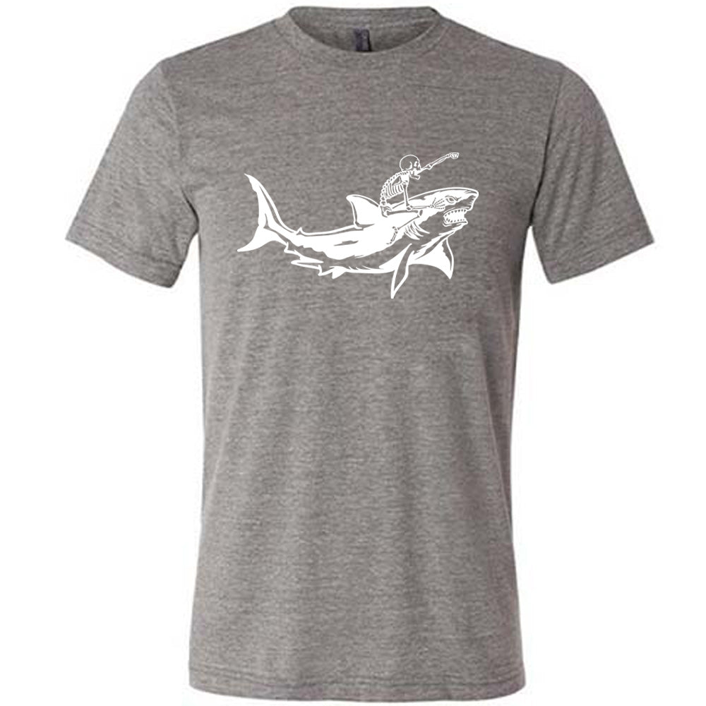 grey unisex tee with the graphic of a skeleton, with its fist pointing onwards and its mouth open, riding a shark, who has a fierce expression