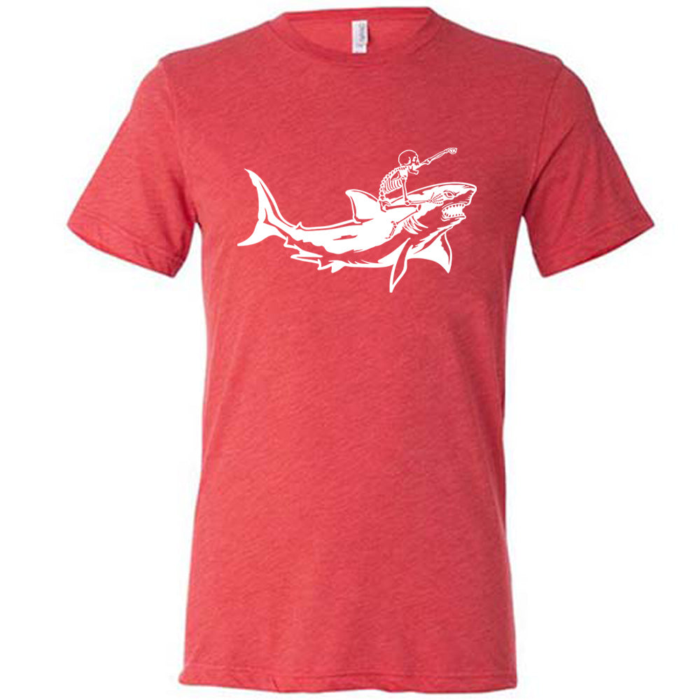 red unisex tee with the graphic of a skeleton, with its fist pointing onwards and its mouth open, riding a shark, who has a fierce expression