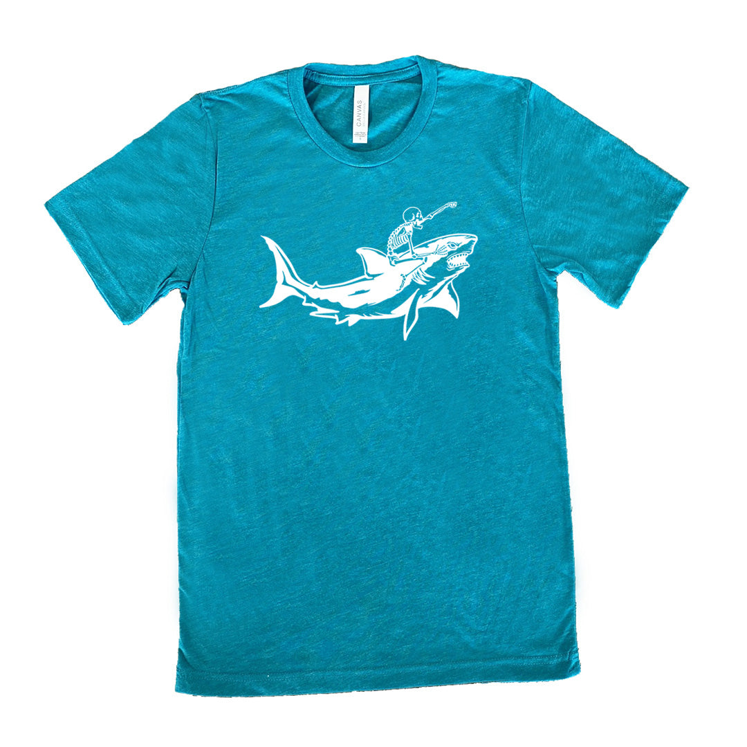 teal unisex tee with the graphic of a skeleton, with its fist pointing onwards and its mouth open, riding a shark, who has a fierce expression