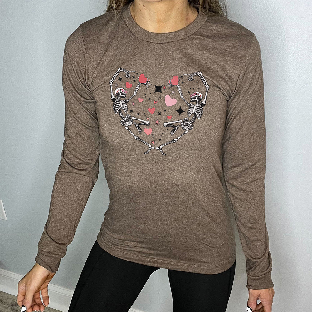 heather brown long sleeve shirt with the graphic of two skeletons creating the shape of a heart with their bodies, appearing to be dancing, with many hearts between them, and a few little stars