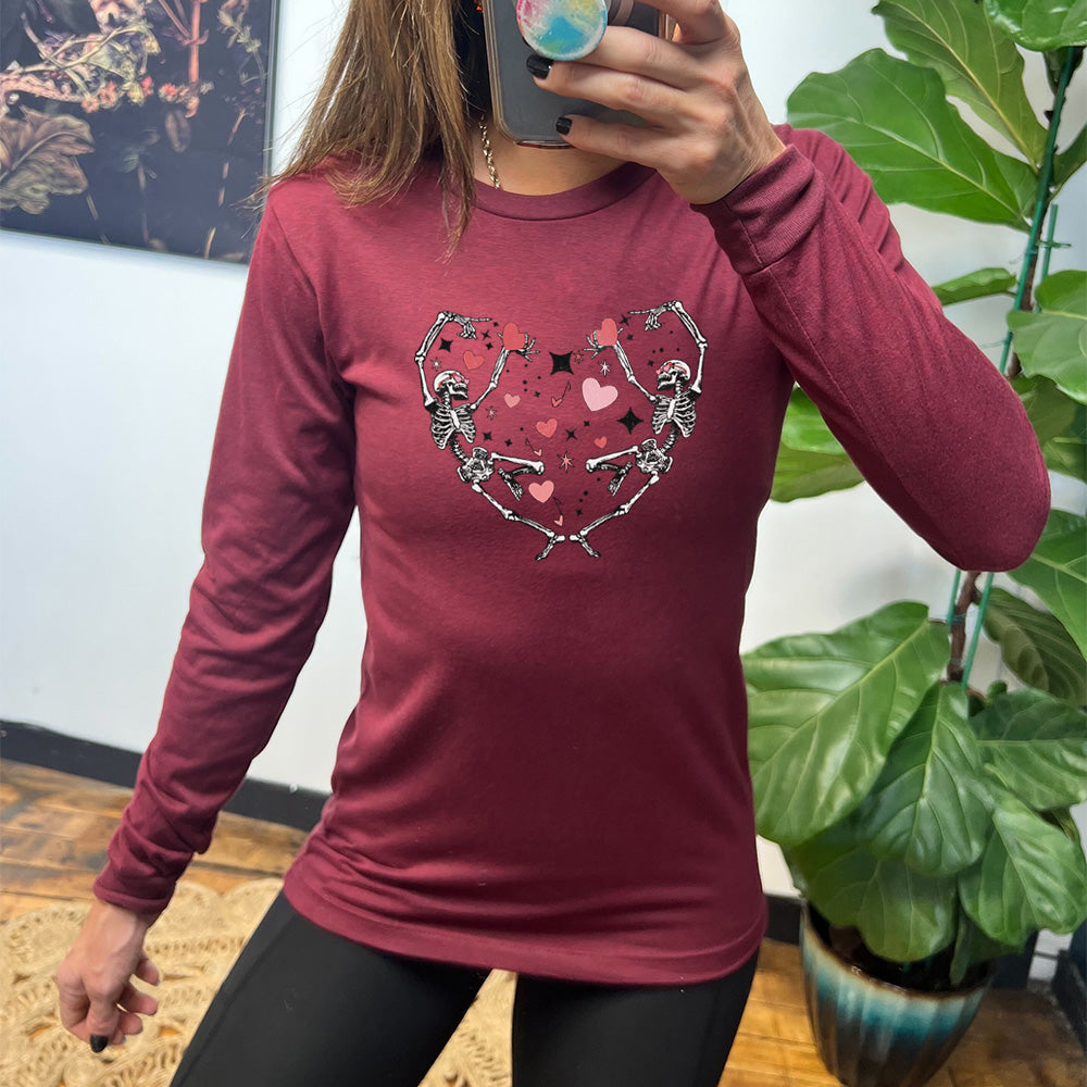 heather cardinal long sleeve shirt with the graphic of two skeletons creating the shape of a heart with their bodies, appearing to be dancing, with many hearts between them, and a few little stars