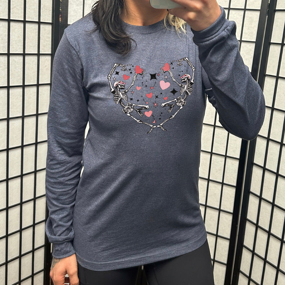heather navy long sleeve shirt with the graphic of two skeletons creating the shape of a heart with their bodies, appearing to be dancing, with many hearts between them, and a few little stars