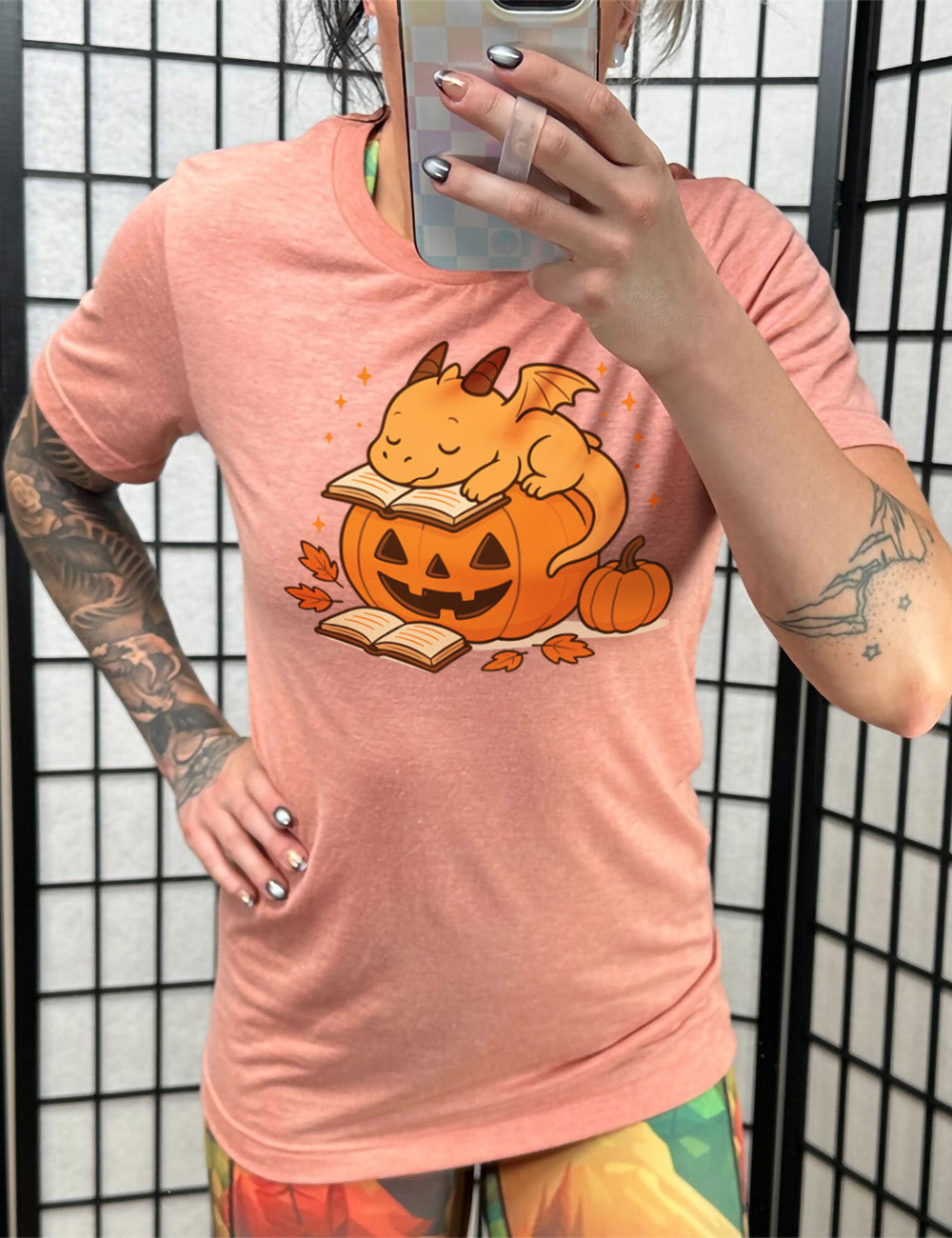 sunset unisex tee with the graphic of a cartoon-style dragon sleeping, with its head in its open book, on top of a jack-o-lantern, with another open book and small pumpkin next to all this, and a scattering of stars, and a few leaves