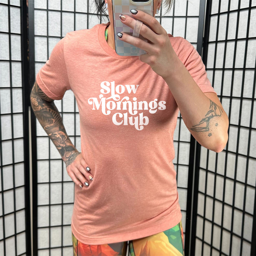 Model wearing sunset colored shirt with a graphic on it that says "Slow Mornings Club" 