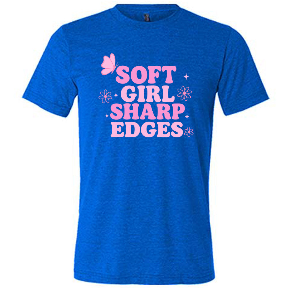 blue unisex tee with the words "soft girl sharp edges" in all caps, with graphics of a few little flowers and stars and one butterfly 