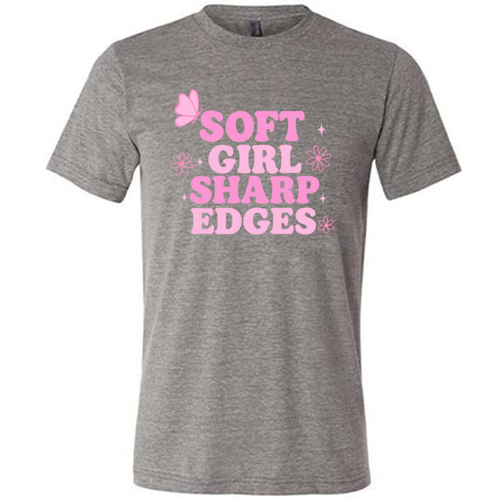 grey unisex tee with the words "soft girl sharp edges" in all caps, with graphics of a few little flowers and stars and one butterfly 