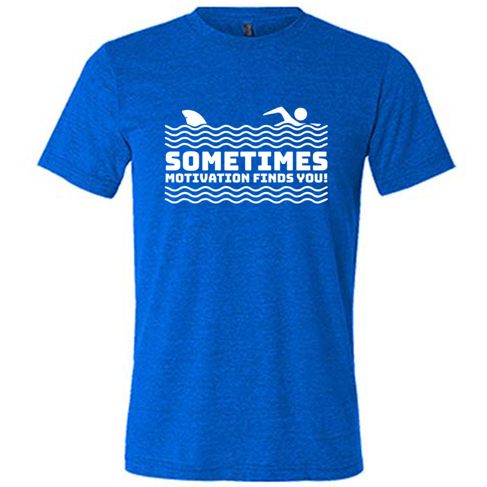 blue unisex tee with the words "sometimes motivation finds you!" in between the lined graphic of waves of the sea, and on top of the waves is the graphic of a figure swimming away from a fin in the water behind