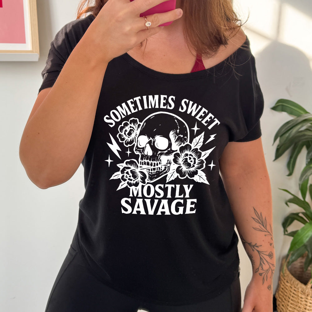 black slouchy tee with the words "sometimes sweet mostly savage on it with the graphic of a skull holding a flower between its teeth, with a couple flowers and a few stars and lightening bolts around it