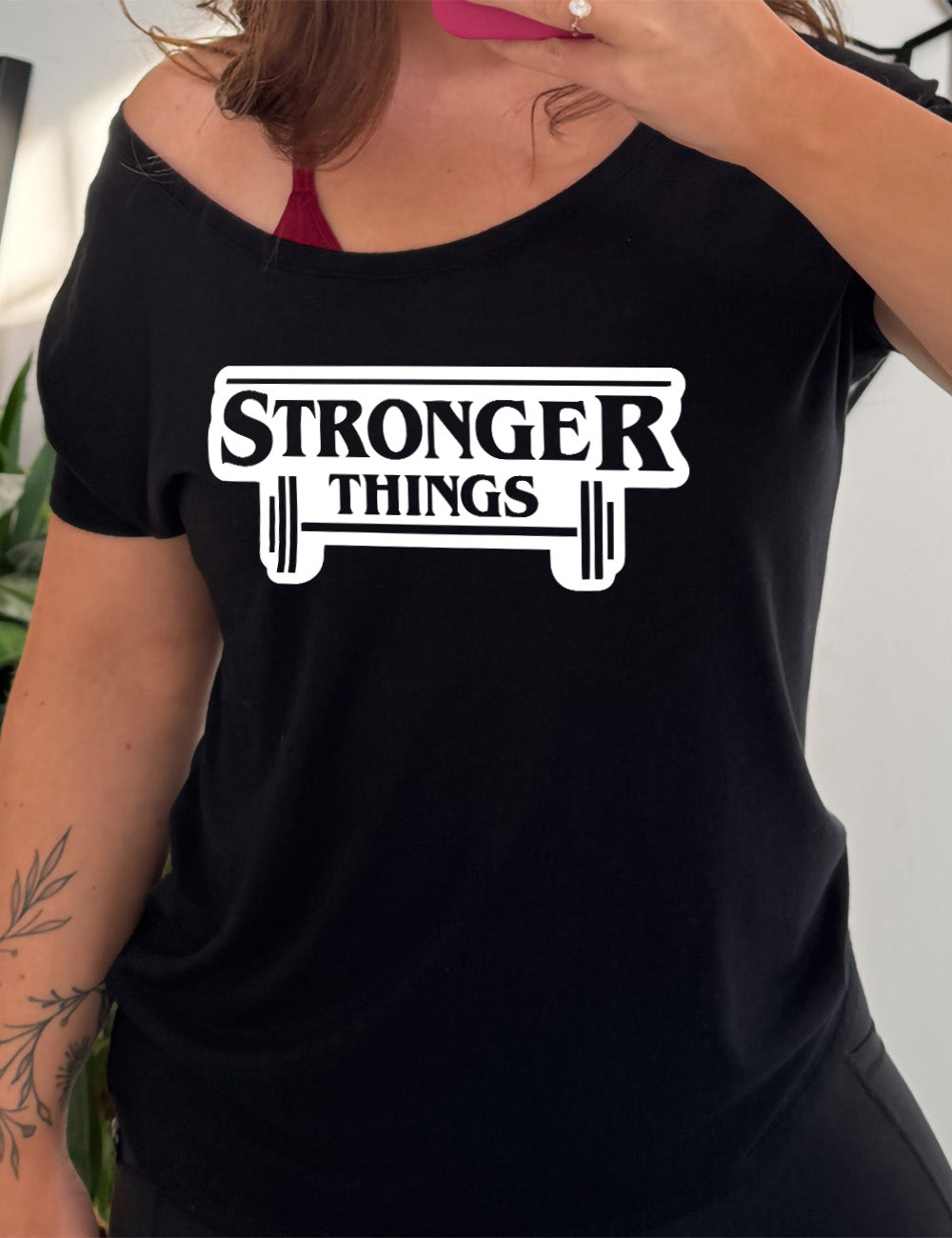 black slouchy tee with the words "stronger things" on it, with a barbell underneath, all in the fashion of the stranger things logo