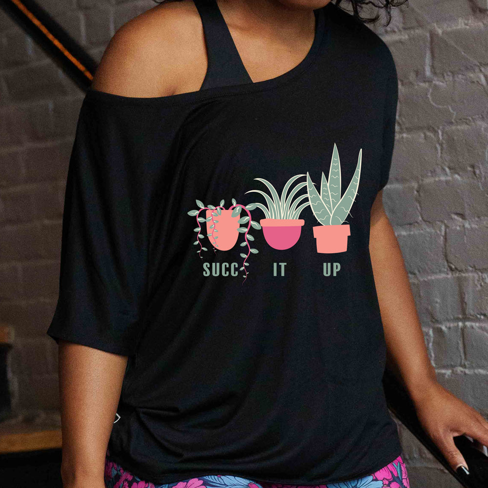 A person wearing a black off-the-shoulder slouchy tee with 'SUCC IT UP' text and illustrations of three potted plants on the front.