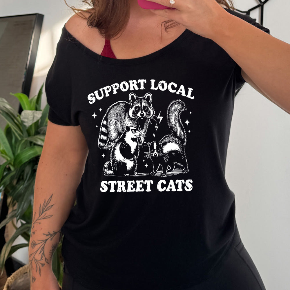 black slouchy tee with the words "support local street cats" and the graphics of a racoon, a skunk, and a possum, all wearing sunglasses, with a few little stars and lightening bolts around