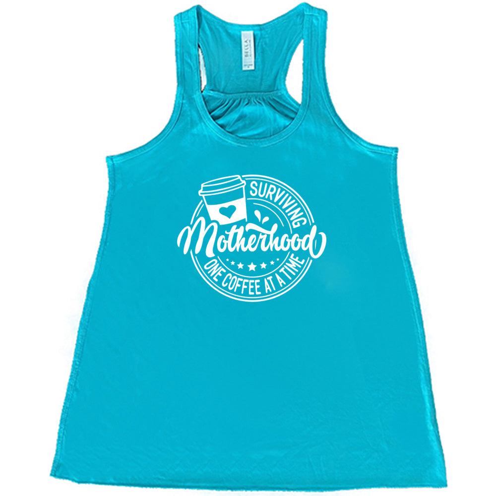 Teal colored flowy tank with a coffee cup graphic on it that says "Surviving Motherhood One Coffee at a Time" 