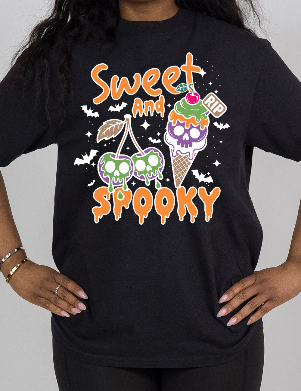 black modern tee with the graphic of two cherries on the same branch, with a skull dripping on each of them, and a cherry-topped ice cream cone, with one of the scoops being a skull, with a little "RIP" sign sticking out of the cone, surrounded by bats and stars, and the words starting on top and ending below the graphics saying "sweet and spooky"