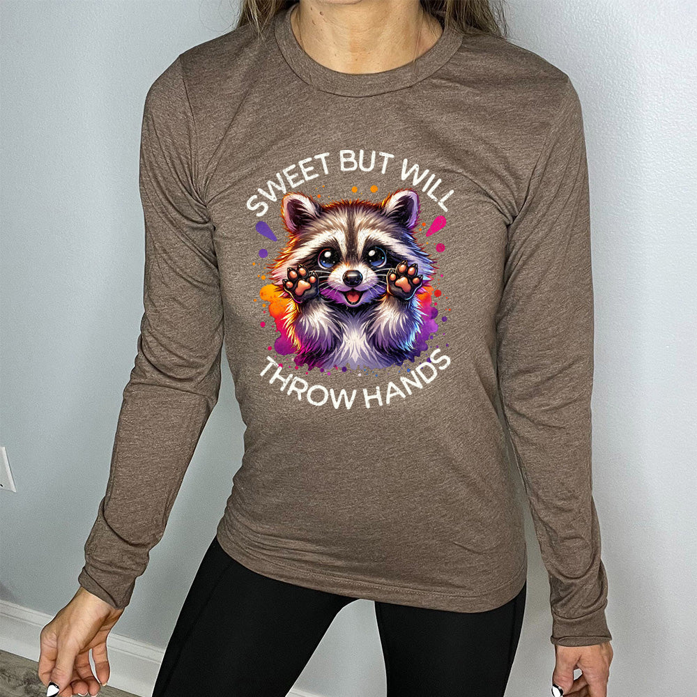 heather brown long sleeve shirt with the words "sweet but will throw hands" on it, with the graphic cartoon of a racoon with innocent-looking eyes, holding up its paws