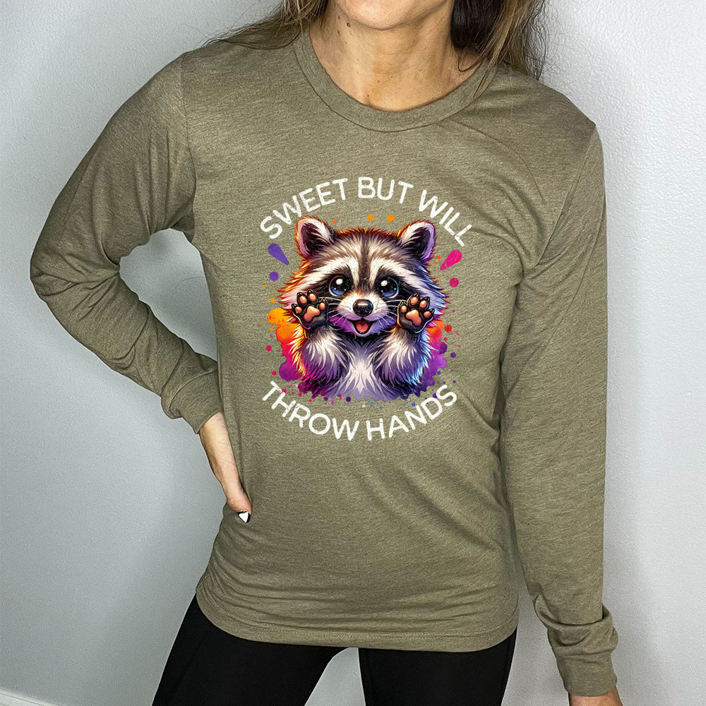heather olive long sleeve shirt with the words "sweet but will throw hands" on it, with the graphic cartoon of a racoon with innocent-looking eyes, holding up its paws