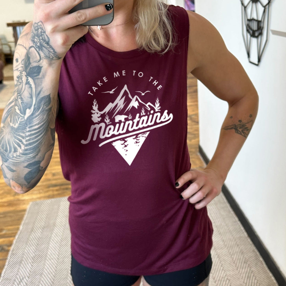 Model wearing maroon colored muscle tank with a mountains graphic on it that says "Take Me To The Mountains"