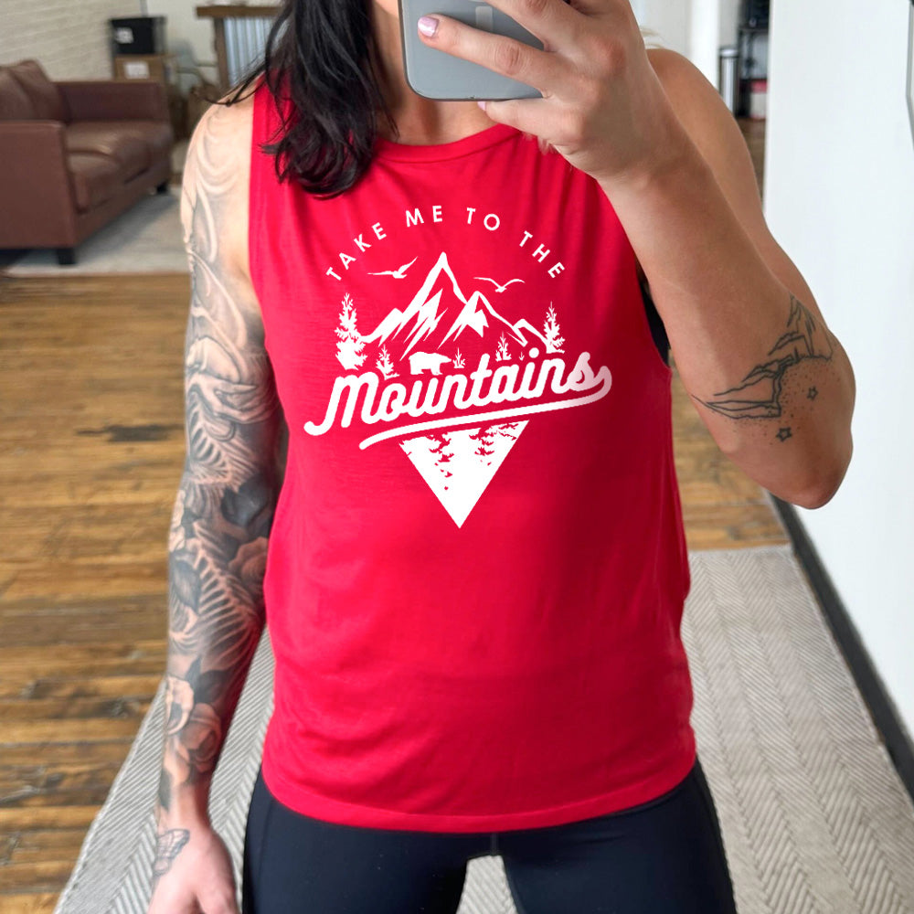 Model wearing red colored muscle tank with a mountains graphic on it that says "Take Me To The Mountains" 