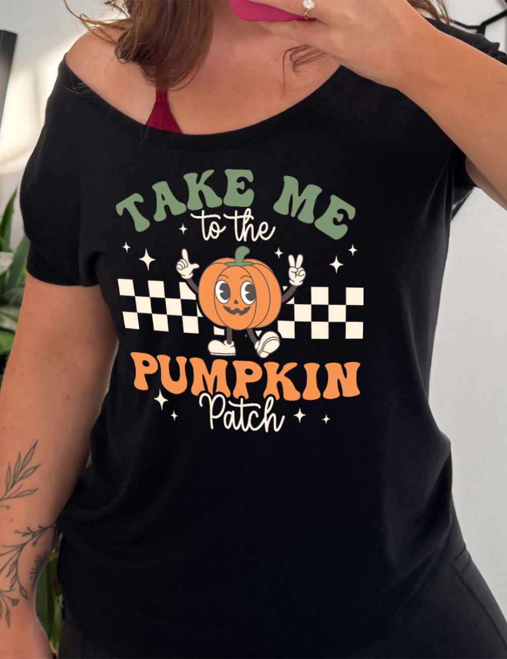 black slouchy tee with the retro design of a pumpkin with arms raised, foot kicked out, in front of a checkered panel, with a few stars around, and the words above and below saying "Take me to the pumpkin patch"