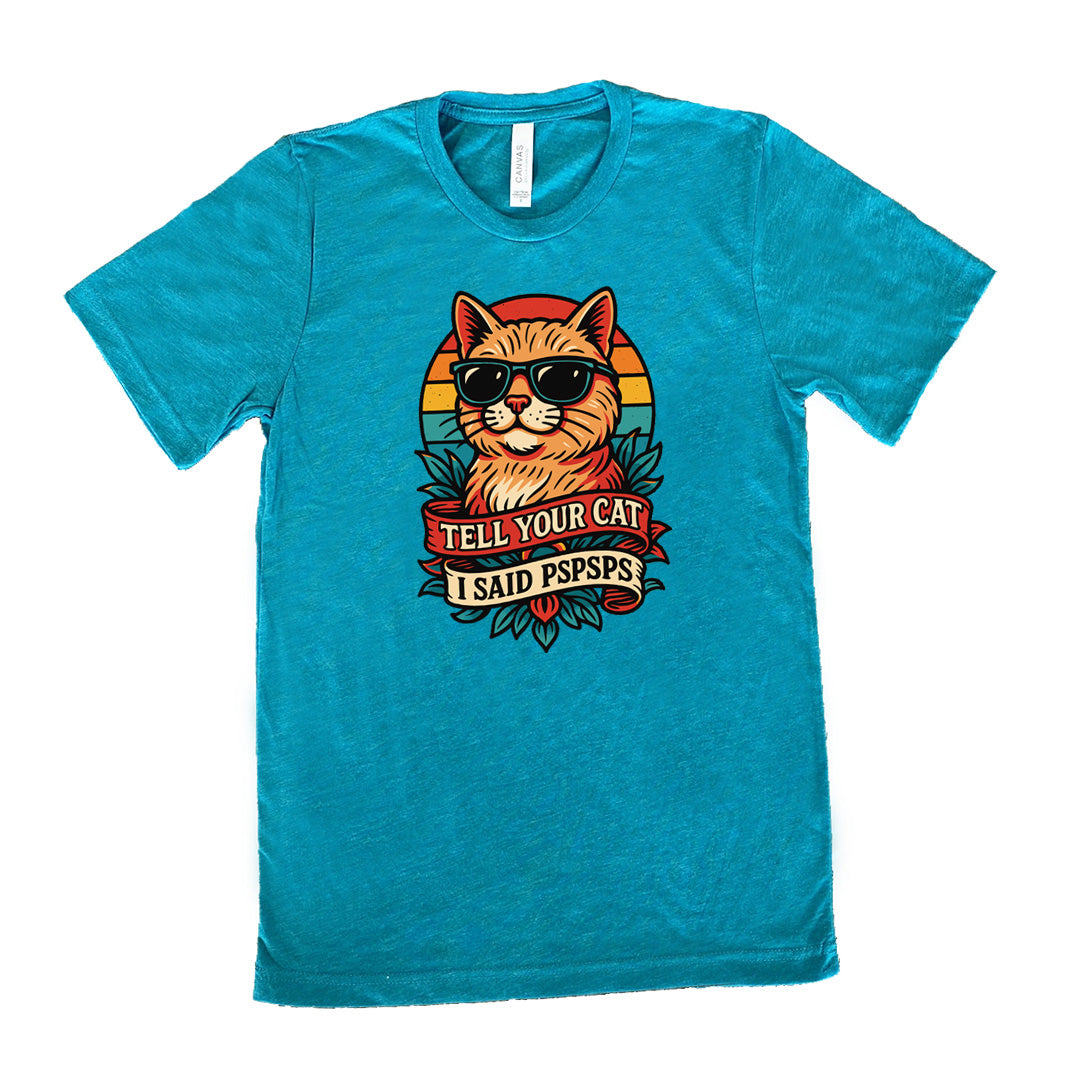 teal unisex tee with the large graphic of a cat head and torso, wearing sunglasses, with a colorful background, and two banners below it with the words "tell your cat I said pspsps" on them