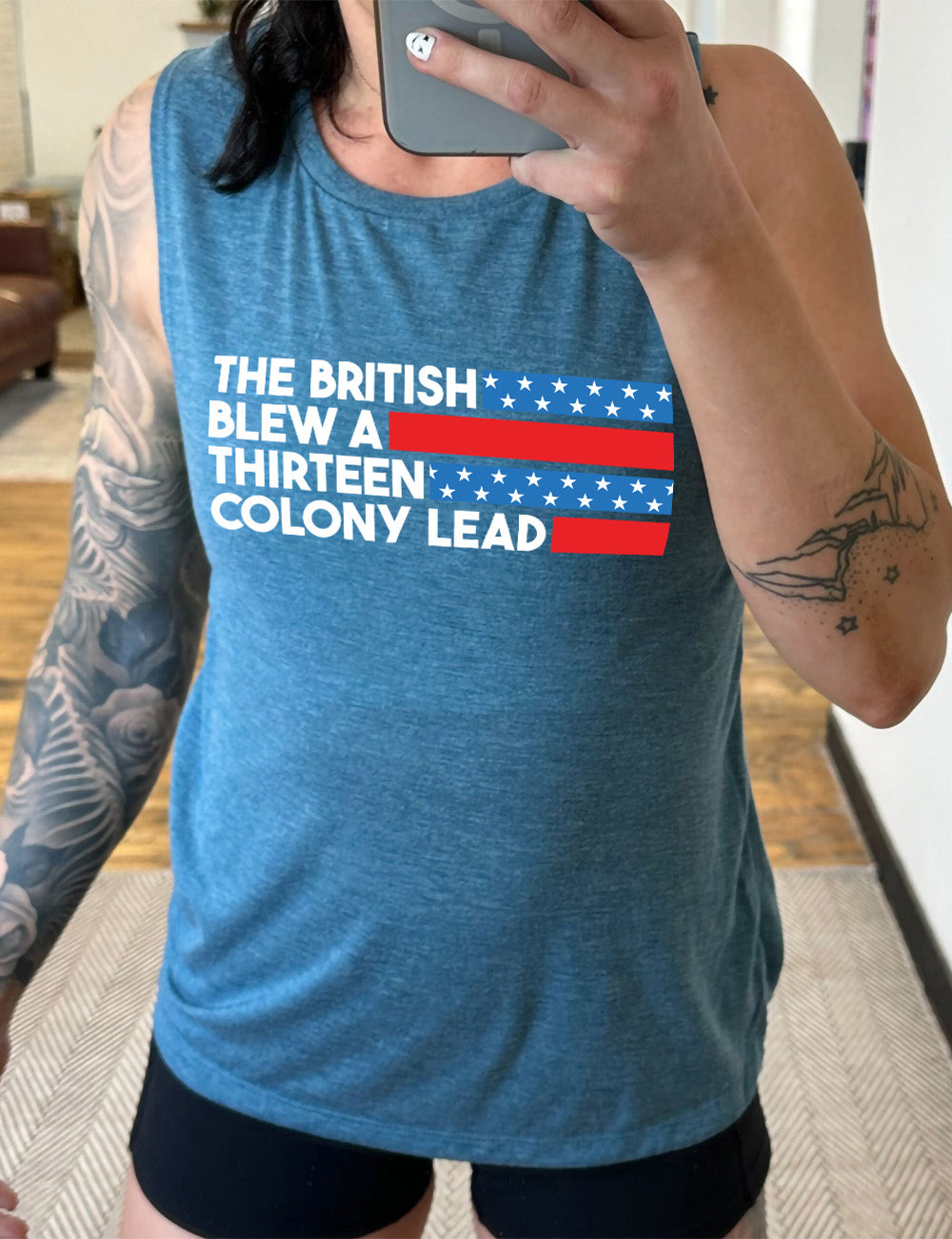 deep teal muscle tank with the words "the British" (and a blue starred bar finishing the space to the right), then below "blew a" (and a red bar), then below "thirteen" (and a blue starred bar),  and below "colony lead" (and a red bar)