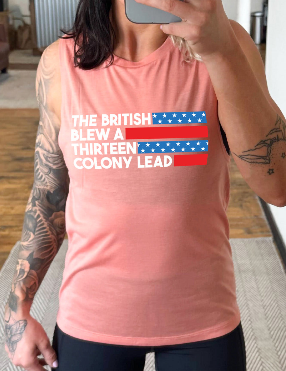 peach muscle tank with the words "the British" (and a blue starred bar finishing the space to the right), then below "blew a" (and a red bar), then below "thirteen" (and a blue starred bar),  and below "colony lead" (and a red bar)
