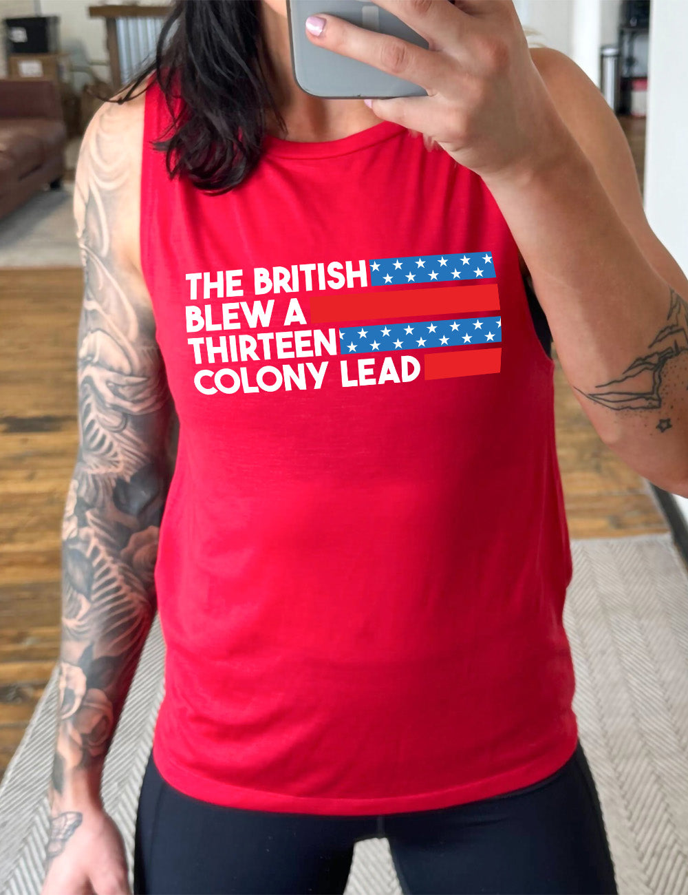 red muscle tank with the words "the British" (and a blue starred bar finishing the space to the right), then below "blew a" (and a red bar), then below "thirteen" (and a blue starred bar),  and below "colony lead" (and a red bar)