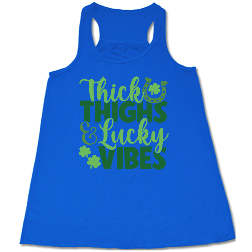blue flowy tank with the words "thick thighs & lucky vibes" on it, with graphics of a horseshoe and a few shamrocks