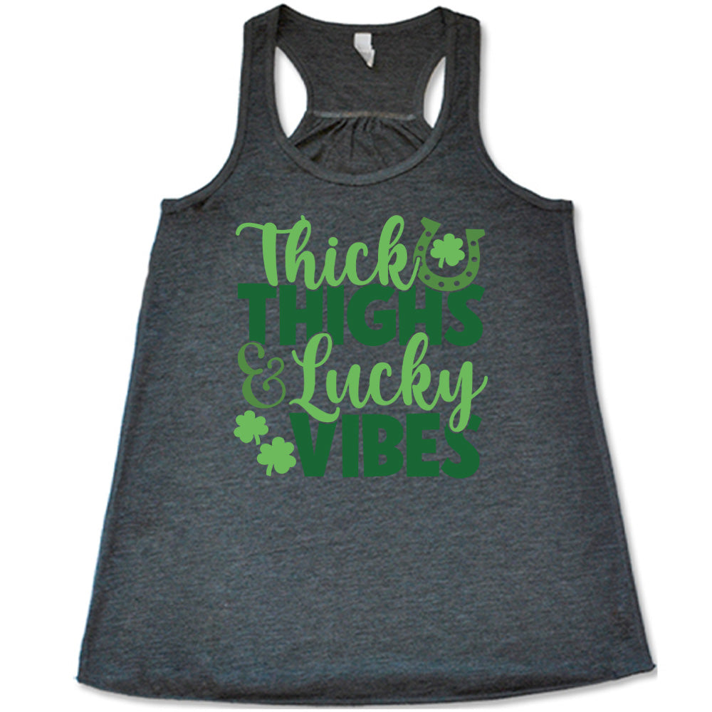 grey flowy tank with the words "thick thighs & lucky vibes" on it, with graphics of a horseshoe and a few shamrocks