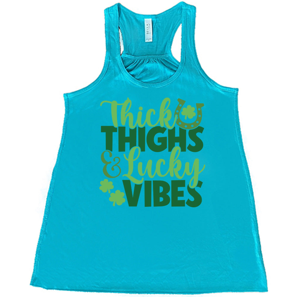 teal flowy tank with the words "thick thighs & lucky vibes" on it, with graphics of a horseshoe and a few shamrocks